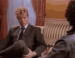 a man in a suit is sitting on a couch talking to another man .