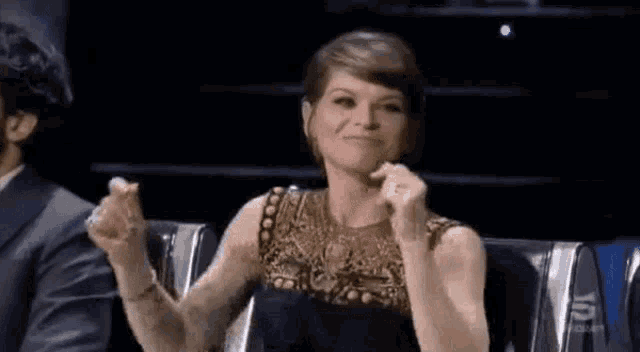 a woman in a black dress is sitting in a chair with her hands up .