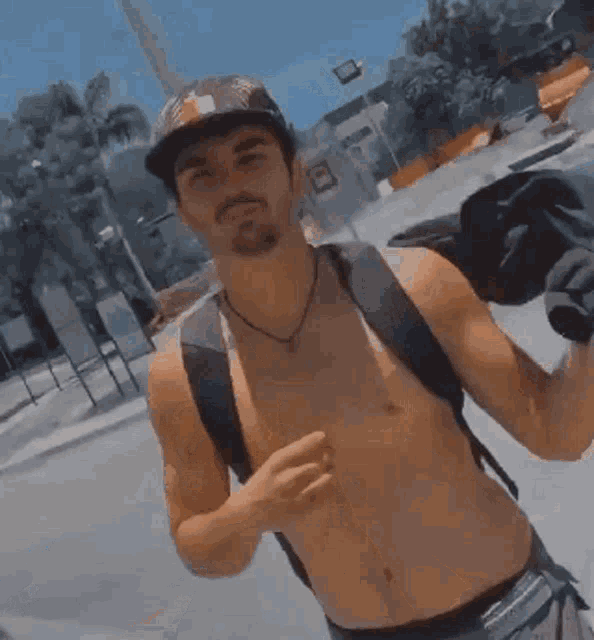 a shirtless man wearing a hat and a backpack is standing on a street