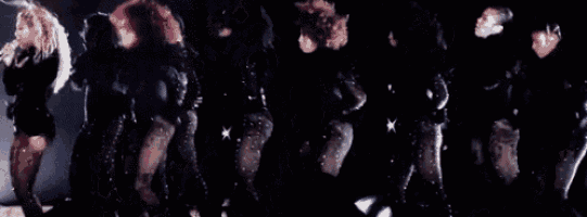 a group of women are dancing on a stage while a woman is singing into a microphone .