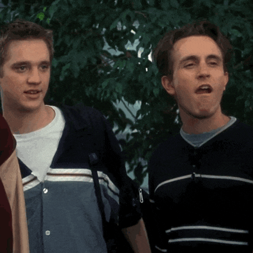 two young men standing next to each other with one wearing a striped sweater