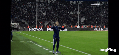 a man stands on a soccer field with ads for nova and petridi in the background