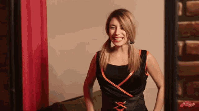 a woman in a black and orange dress is smiling and standing in front of a red curtain