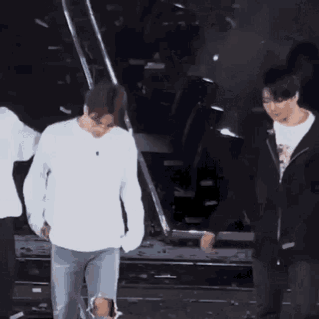 two men are standing next to each other on a stage holding hands . one of the men is wearing ripped jeans .