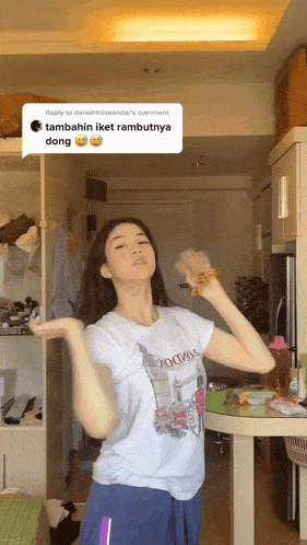 a woman in a white t-shirt is dancing in a kitchen with a reply to danishbriskandar 's comment