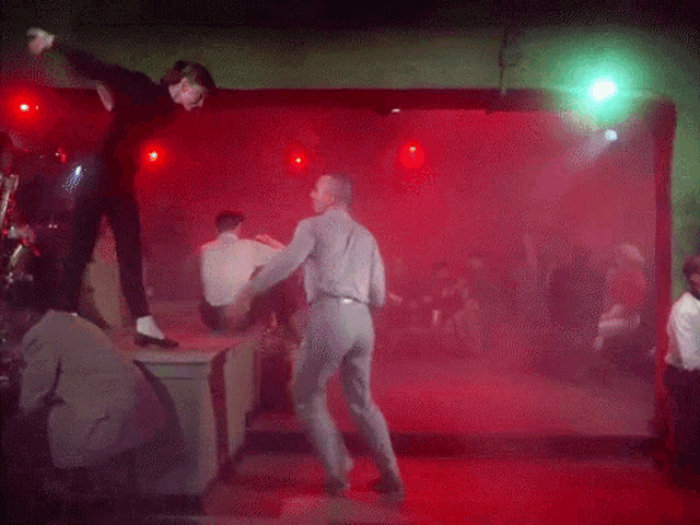 a group of people dancing in a dark room with red lights
