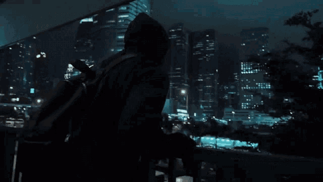 a man standing on a balcony looking out at a city at night