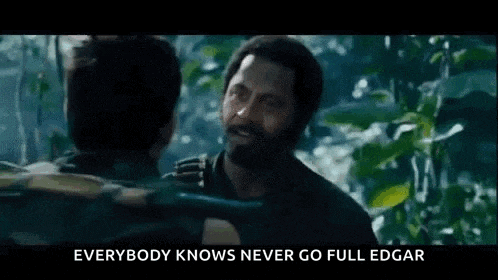 a man with a beard is talking to another man in a forest .