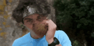 a man wearing a headband and a blue shirt is eating a pear .