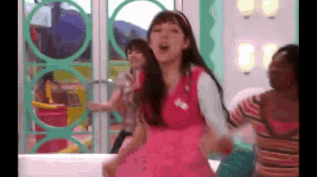 a girl in a pink dress is dancing in a room with two other girls .