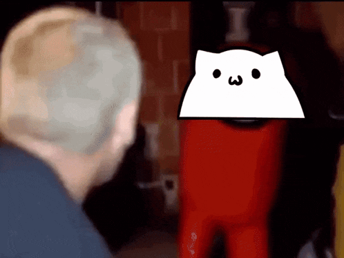 a man is standing in front of a red among us character with a white cat on its head .