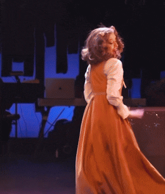 a woman in a long brown dress is dancing on stage