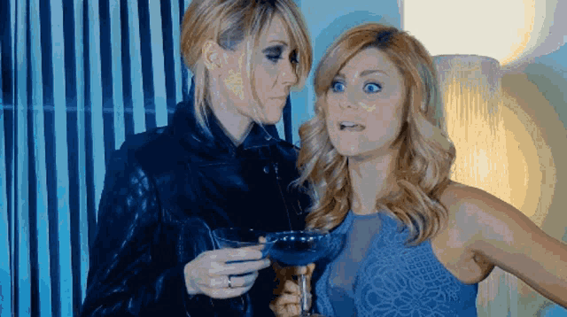 two women are standing next to each other and one is holding a glass of wine