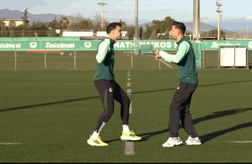 two soccer players are standing on a field with a sign that says ' nationikos ' on it