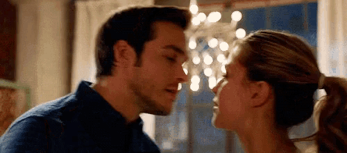 a man and a woman are kissing in front of a chandelier in a living room .