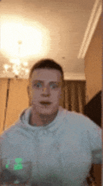 a man in a white hoodie is holding a glass of water in a living room .