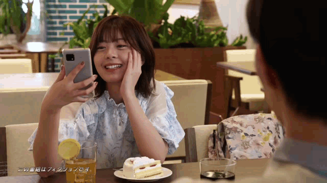 a woman sitting at a table with a plate of cake and a cell phone