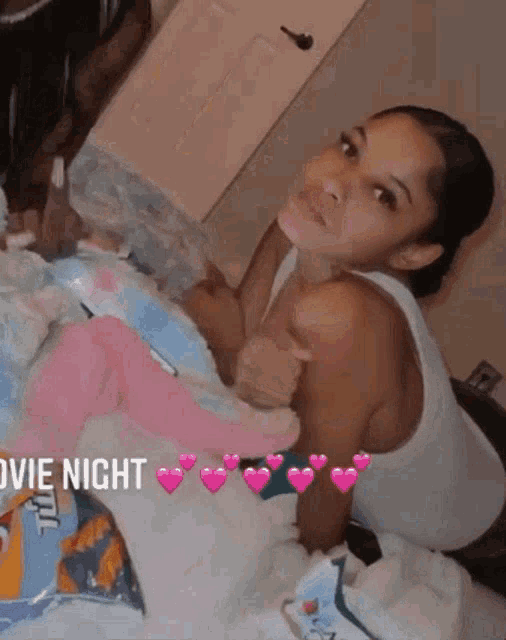 a woman in a white tank top is laying on a bed with a baby in her arms .