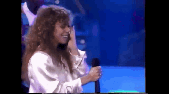 a woman is singing into a microphone while wearing a white shirt .