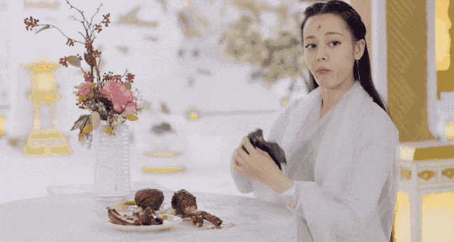 a woman in a white dress is standing in front of a table with plates of food and a vase of flowers