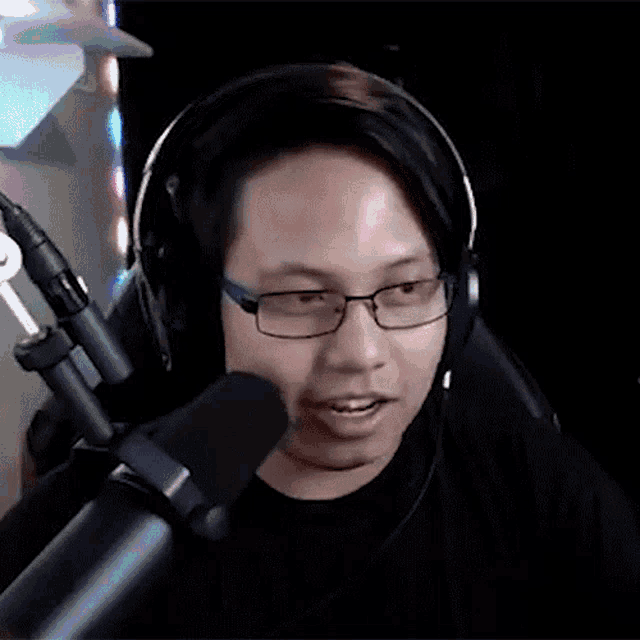 a man wearing headphones and glasses is speaking into a microphone .