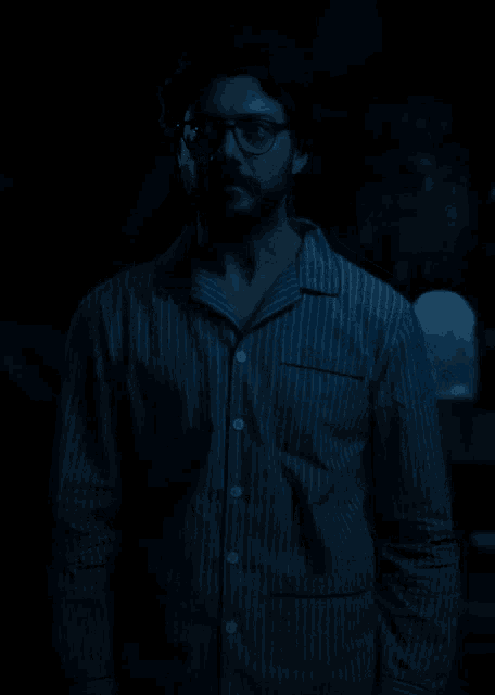 a man in a striped shirt and glasses stands in the dark