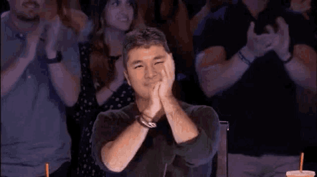 a man is clapping his hands while sitting in front of a crowd .