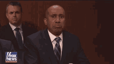 a man in a suit and tie is sitting in front of a fox news channel sign