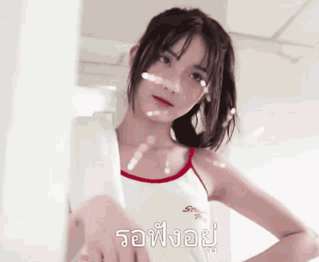 a girl in a white tank top is standing in front of a white wall with a foreign language written on it ..