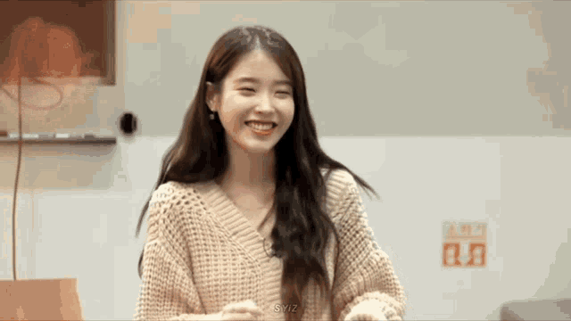 a young woman wearing a sweater is smiling and looking at the camera .
