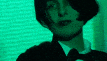 a woman wearing a tuxedo and bow tie is standing in front of a green screen .