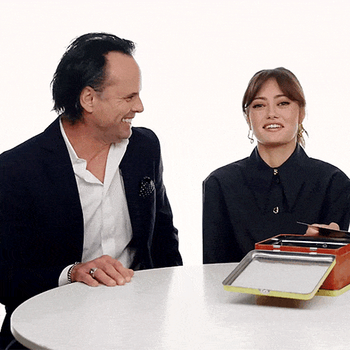a man and a woman are sitting at a table and the woman is holding a box with the number 3 on it