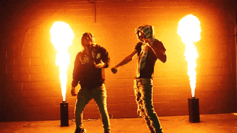 two men are standing in front of a wall with fire coming out of them