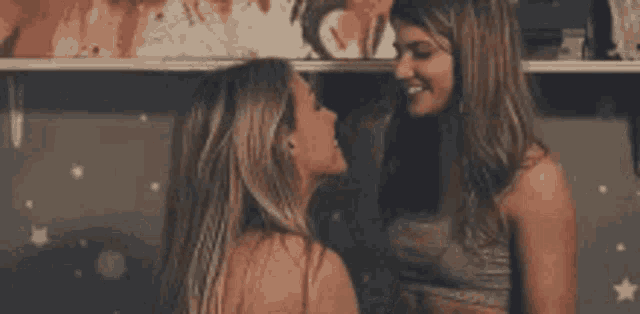two women are kissing each other in front of a wall .