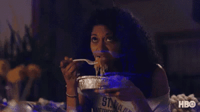 a woman is sitting on a bed eating noodles from a tin foil pan .