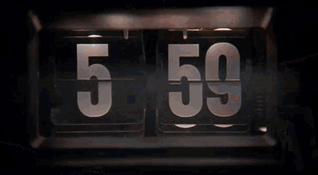 a man is laying in bed next to a flip clock that shows the time as 6:00 .