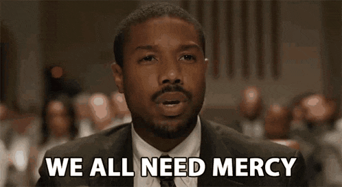 a man in a suit and tie is sitting in front of a crowd and says `` we all need mercy '' .