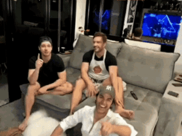 three men are sitting on a couch with one wearing an apron that says ny