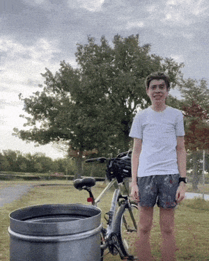 a young man stands in front of a bicycle and a trash can
