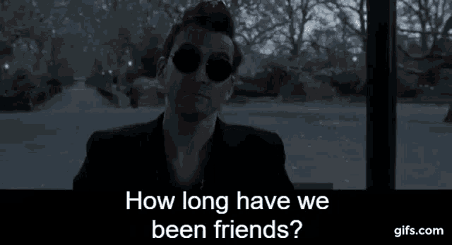 a man wearing sunglasses is sitting in front of a window and talking about how long have we been friends .