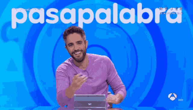 a man in a purple shirt is sitting in front of a blue background that says pasapalabra