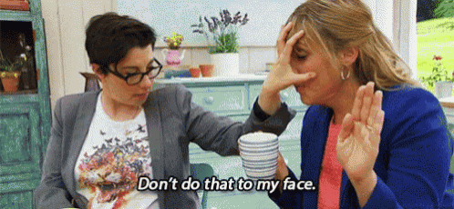 two women are sitting at a table talking to each other and one of them is covering her nose .