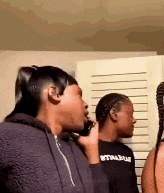 a woman is talking on a cell phone while standing next to another woman in a room .