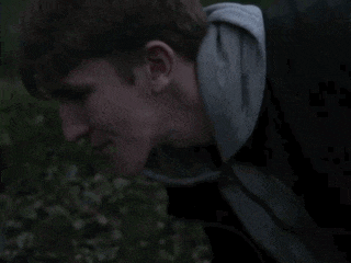 a man in a hoodie is standing in a field looking at something .
