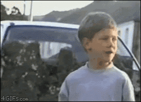 a young boy is standing in front of a car with his mouth open