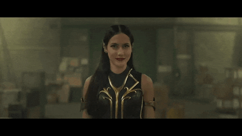a woman in a black and gold superhero costume is standing in a dark room .