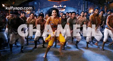 a woman is dancing in front of a crowd of people with the word chameen written in the background .