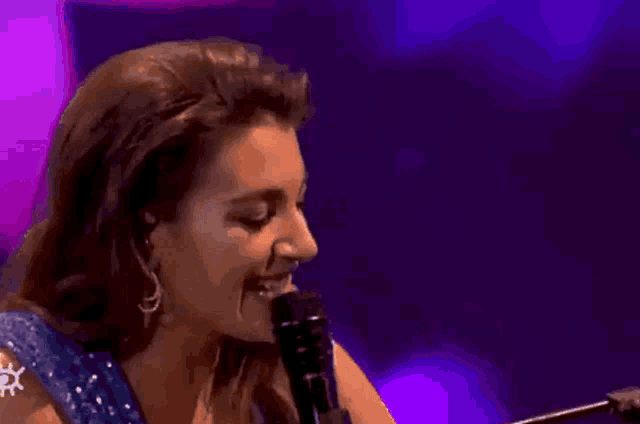 a woman in a blue dress is laughing while holding a microphone .