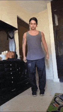 a man wearing a gray tank top and black pants with the word love on them is standing in front of a dresser