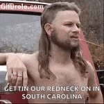 a shirtless man with a mullet and a beard is standing in front of a car in south carolina .